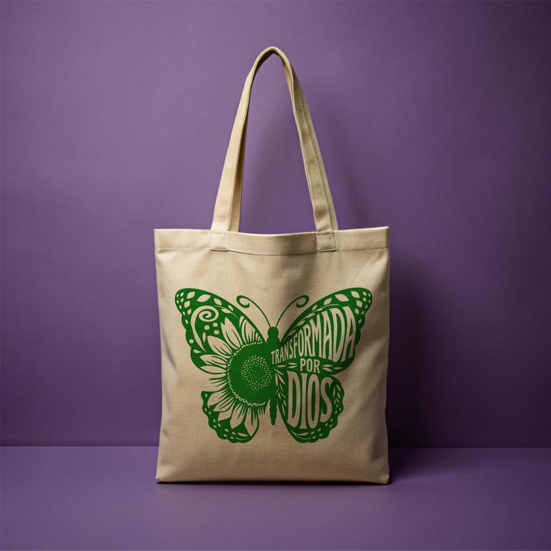 May include: A beige canvas tote bag with green butterfly design. The butterfly has a sunflower in the center and the text "TRANSFORMADA POR DIOS" inside the wings.