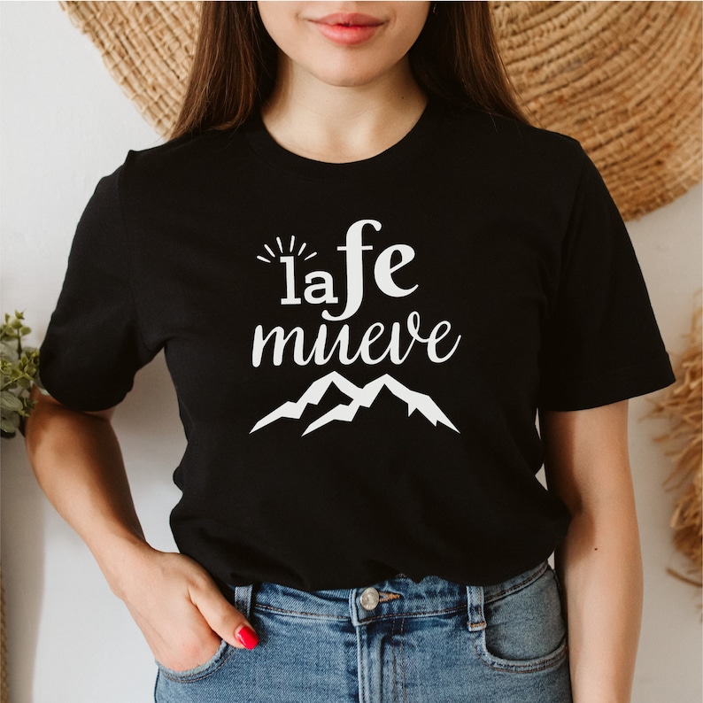 May include: Black t-shirt with white text that reads "la fe mueve" and a graphic of mountains.