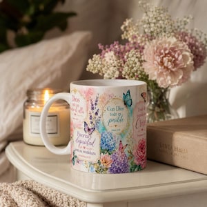 May include: White ceramic mug with floral and butterfly designs, and text in Spanish. The mug has a handle and is on a white surface next to a candle and a vase of flowers. A book is also visible.