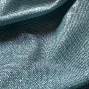 May include: Close-up of a soft, blue fabric with a subtle shimmer. The fabric has a textured, ribbed surface.
