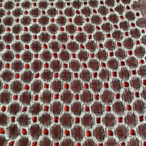 Peut inclure: Gros plan sur un tissu avec un motif r&eacute;p&eacute;titif de petits cercles rouges dans un design hexagonal blanc. Le tissu a une apparence textur&eacute;e, presque matelass&eacute;e.