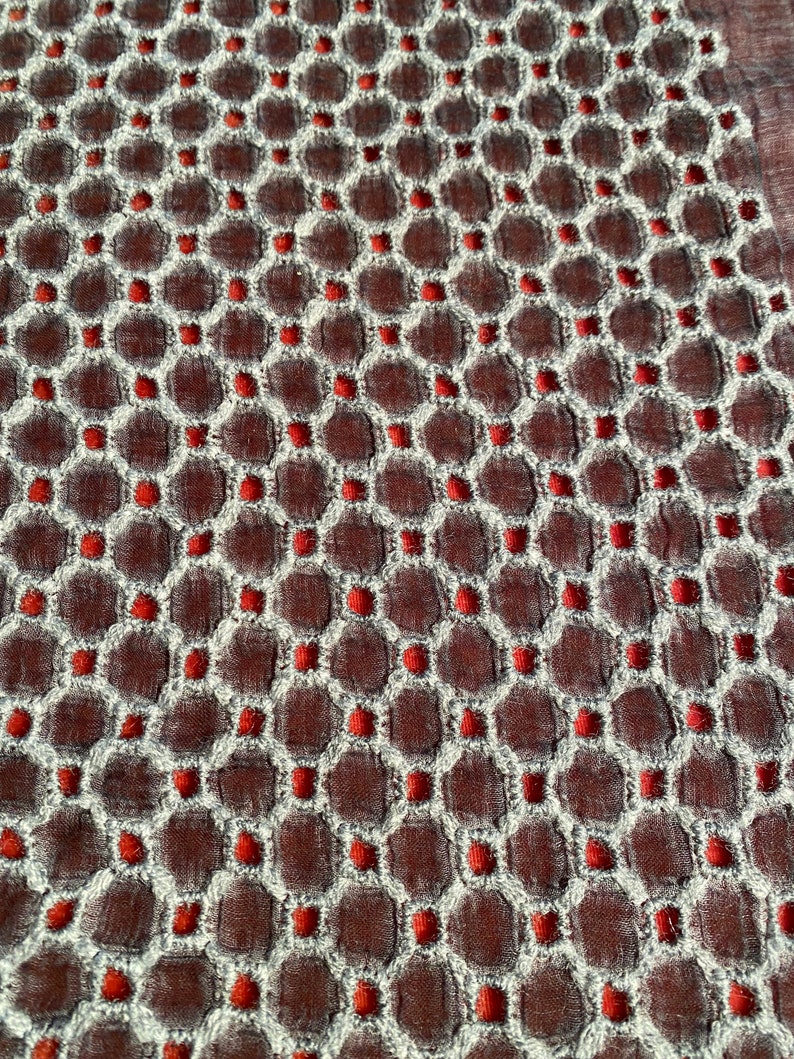 Peut inclure: Gros plan sur un tissu avec un motif r&eacute;p&eacute;titif de petits cercles rouges dans un design hexagonal blanc. Le tissu a une apparence textur&eacute;e, presque matelass&eacute;e.