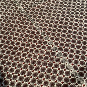 Peut inclure: Gros plan sur un tissu avec un motif g&eacute;om&eacute;trique r&eacute;p&eacute;titif. Le motif est compos&eacute; de petits cercles blancs et de points rouges, dispos&eacute;s en grille. Le tissu a une surface textur&eacute;e.