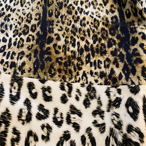 May include: A close-up of a fabric with a leopard print pattern. The fabric is brown, black, and white. The print is a classic leopard print with spots and stripes.