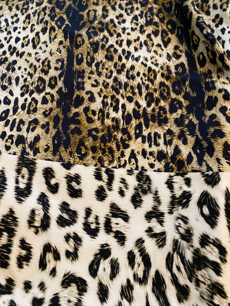 May include: A close-up of a fabric with a leopard print pattern. The fabric is brown, black, and white. The print is a classic leopard print with spots and stripes.