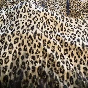 May include: A close-up of a fabric with a leopard print pattern. The fabric is brown, black, and white. The print is a classic leopard print with black spots on a brown background.