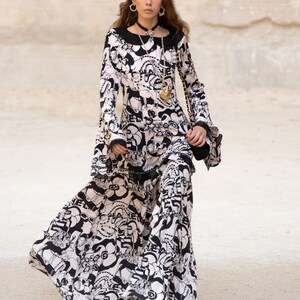 Peut inclure: Une femme portant une robe &agrave; motifs noir et blanc &agrave; manches longues et une jupe ample. Elle porte un collier en or avec un pendentif en forme de c&oelig;ur et des bottes &agrave; talons blanches.
