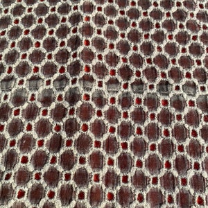 Peut inclure: Gros plan sur un tissu avec un motif r&eacute;p&eacute;titif de cercles blancs et de points rouges sur un fond brun fonc&eacute;.
