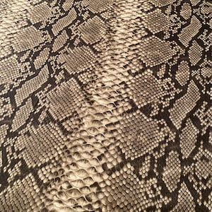 May include: Close-up of a brown and beige snakeskin pattern. The pattern is made up of small, overlapping scales.