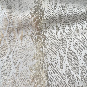 May include: A fabric featuring a metallic silver and gold snakeskin pattern. The material displays a repeating reptilian scale texture with a shimmering finish, characterized by alternating light and dark tones across the surface of the textile.
