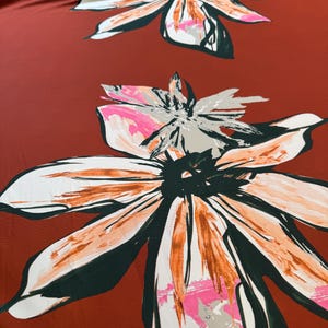 May include: A close-up of a fabric with a large floral pattern. The flowers have white, orange, pink, and dark green accents against a deep red-brown background. The design is repeated across the fabric.