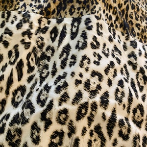May include: Close-up of a fabric with a leopard print pattern. The fabric is white with black and brown spots.