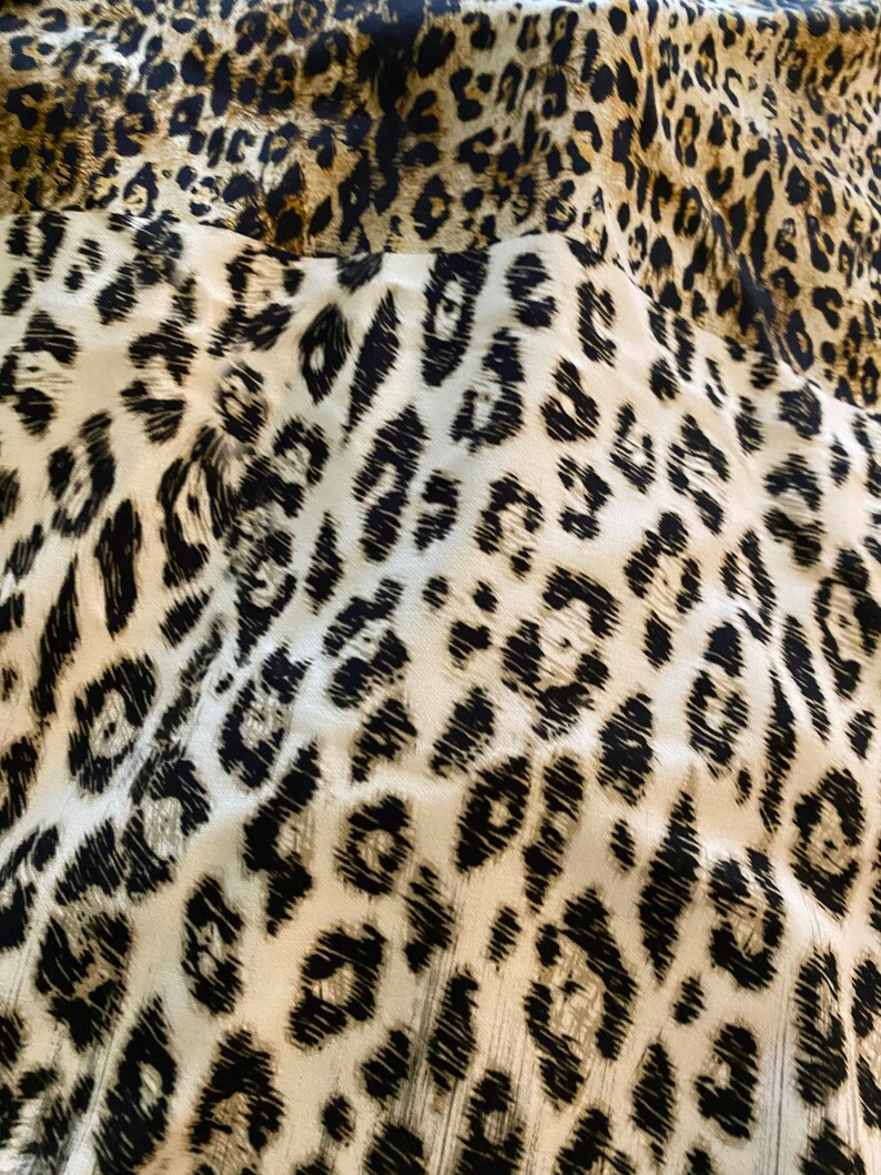 May include: Close-up of a fabric with a leopard print pattern. The fabric is white with black and brown spots.
