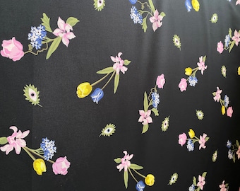 May include: Black fabric with a repeating floral pattern. The flowers are pink, yellow, and blue. The background is black.