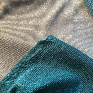 May include: Close-up of two fabric swatches. The top swatch is a light silver color with a subtle shimmer. The bottom swatch is a teal blue color with a shimmer.