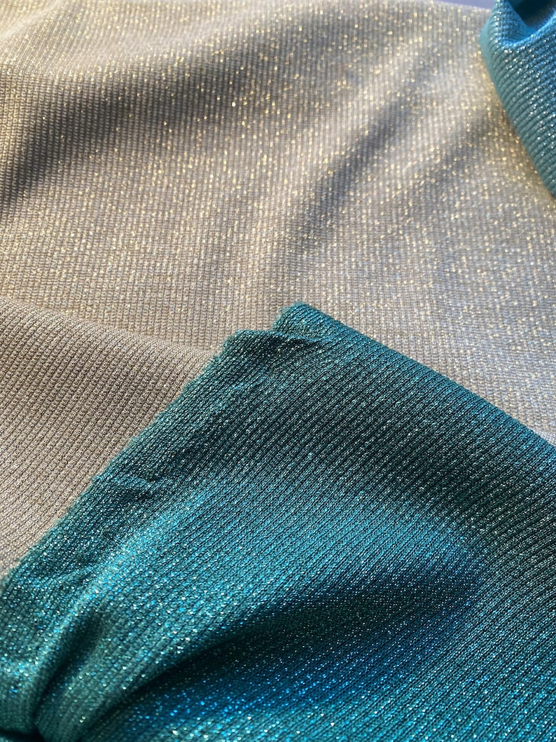 May include: Close-up of two fabric swatches. The top swatch is a light silver color with a subtle shimmer. The bottom swatch is a teal blue color with a shimmer.