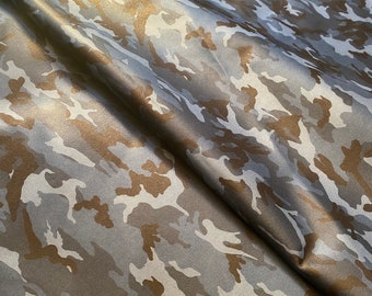 May include: A close-up of a blue and brown camouflage fabric. The fabric has a subtle sheen and is made of a soft, smooth material.
