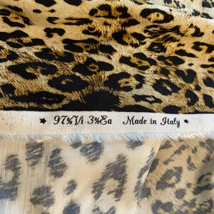 May include: Close-up of a fabric swatch with a leopard print pattern. The fabric is beige with black spots. The label reads "97% Vi - 3% Ea Made in Italy".