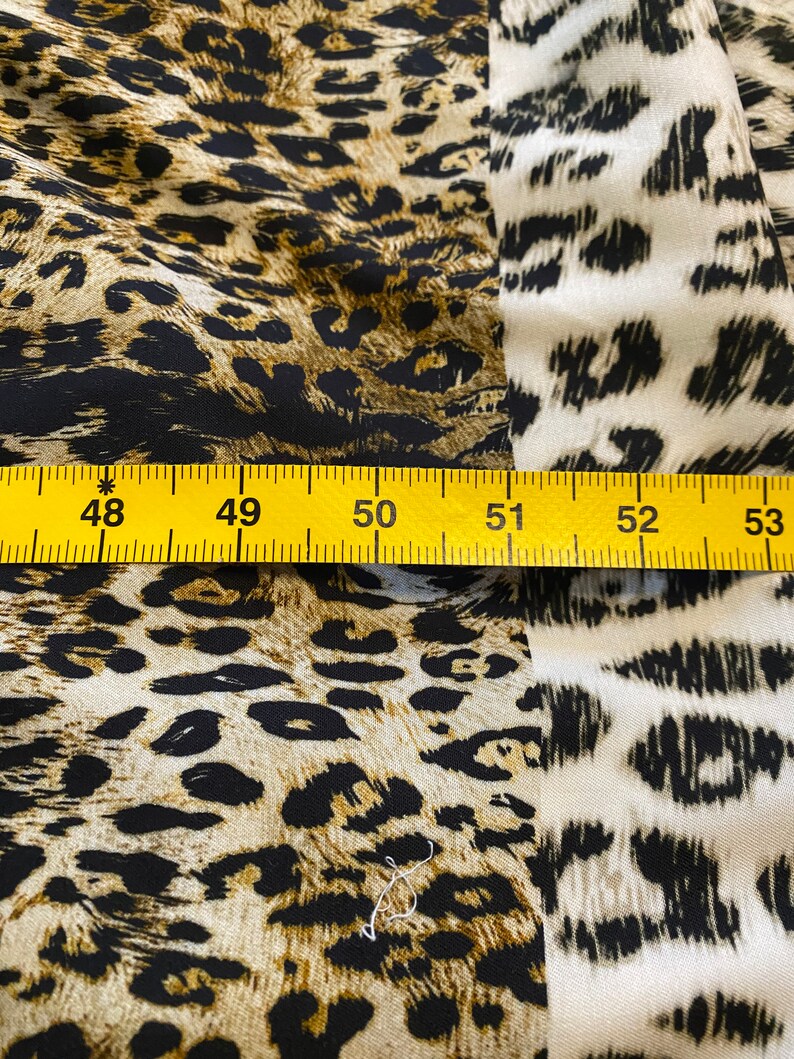 May include: Close-up of a yellow measuring tape with black markings, showing the numbers 48 to 53. The tape is placed on top of a fabric with a brown and black leopard print pattern.