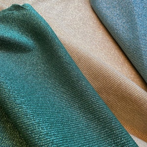 May include: Three fabric swatches in different colors: a deep teal green, a light beige, and a light blue. The fabric has a subtle shimmer and a ribbed texture.