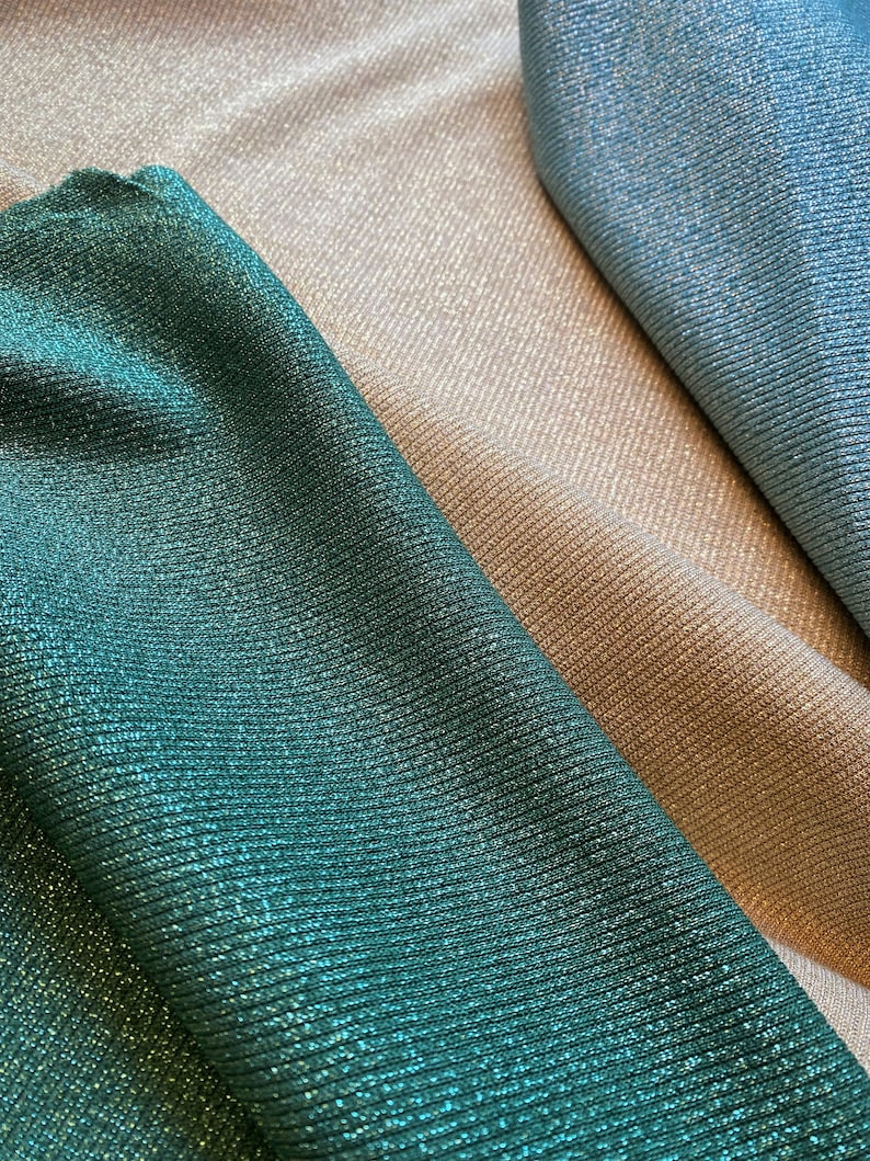 May include: Three fabric swatches in different colors: a deep teal green, a light beige, and a light blue. The fabric has a subtle shimmer and a ribbed texture.
