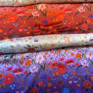 Puede incluir: Primer plano de tres rollos de tela floral. El rollo superior es crema con un estampado floral. El rollo del medio es rojo intenso con flores naranjas y rosas. El rollo inferior es un degradado púrpura con flores naranjas y blancas.