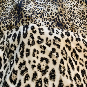 May include: Close-up of a fabric with a leopard print pattern. The fabric is brown, black, and white. The print is a classic leopard print with black spots on a brown background.
