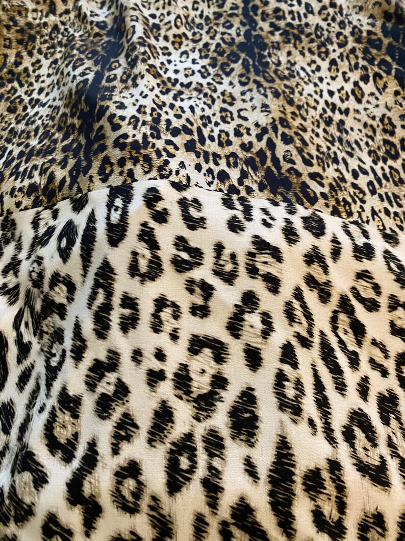 May include: Close-up of a fabric with a leopard print pattern. The fabric is brown, black, and white. The print is a classic leopard print with black spots on a brown background.