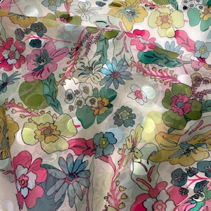 May include: A sheer fabric with a vibrant floral pattern. The design features large, stylized flowers in shades of pink, yellow, blue, and green, set against a light background. The fabric has a delicate, flowing appearance, suggesting it could be used for apparel or home decor.
