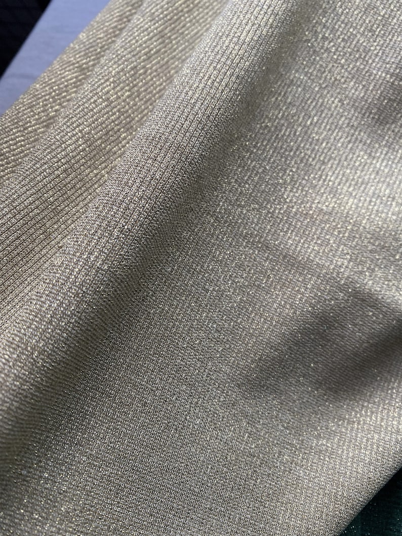 May include: Close-up of a shimmery gold fabric with a ribbed texture. The fabric has a subtle sparkle and a soft, drapey feel.