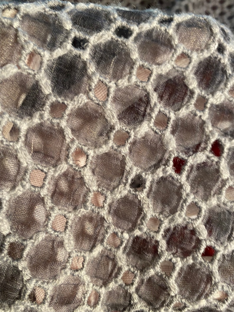 Peut inclure: Gros plan sur un tissu gris et blanc avec un motif r&eacute;p&eacute;titif de petits trous ronds. Le tissu a un aspect textur&eacute; et tiss&eacute;.