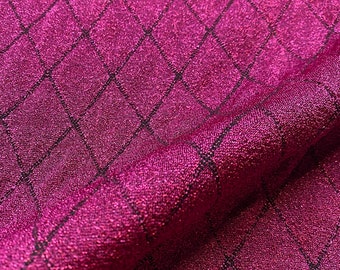 May include: Close-up of a shimmering magenta fabric with a diamond grid pattern. The fabric has a textured surface and a metallic sheen, reflecting light. The grid lines are black, creating a contrast against the magenta background.