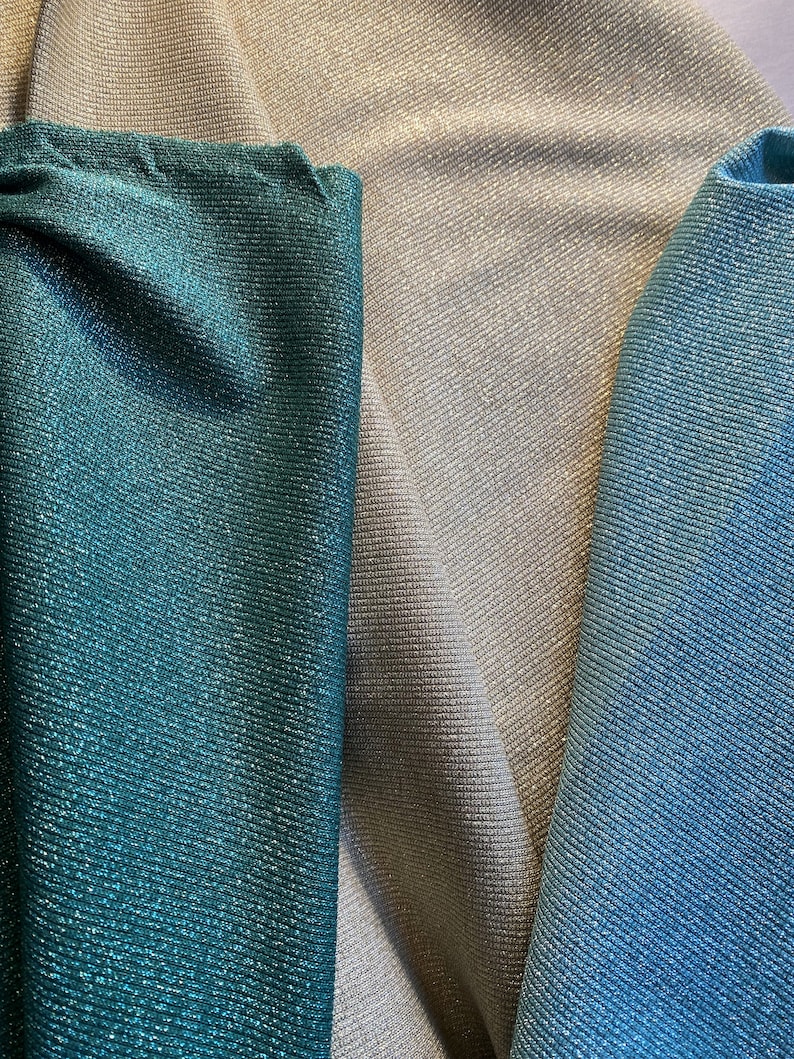 May include: Close-up of three fabric swatches in teal, silver, and light blue. The fabrics have a subtle shimmer and a textured weave.