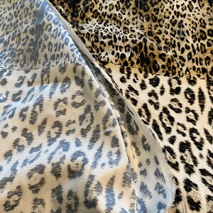 May include: Close-up of a fabric with a leopard print pattern. The fabric is a mix of brown, black, and white.