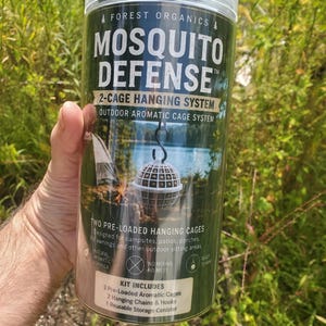 Könnte beinhalten: Ein zylindrischer Behälter aus klarem Kunststoff mit der Aufschrift Forest Organics Mosquito Defense 2-Cage Hanging System. Das Etikett zeigt weißen Text auf dunkelgrünem Hintergrund und beschreibt zwei vorgefüllte Hängekäfige, Ketten und Haken.