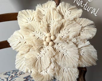 May include: A 16 inch natural macrame flower wall hanging with a wooden bead center. The flower is made with a cream colored cord and has a fringe around the edges.