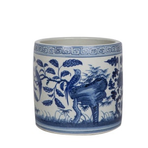 May include: A white ceramic cylinder vase with a blue and white floral design. The vase features a repeating geometric pattern around the top rim and a scene of birds perched on branches with leaves.