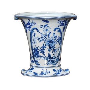 May include: A white ceramic vase with a blue floral pattern. The vase has a wide mouth and a narrow base.
