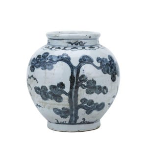 May include: A white ceramic vase with a blue and white design of a tree with branches and leaves. The vase has a round body and a narrow neck.