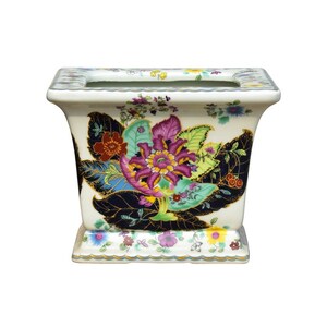 May include: A white ceramic planter with a square shape and a floral design. The planter features a large, colorful flower with green leaves and gold accents. The design is reminiscent of traditional Chinese porcelain.