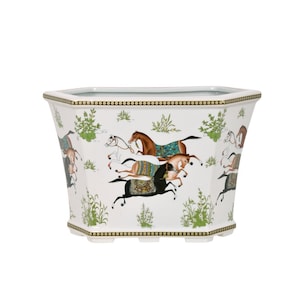 May include: White porcelain planter with a hexagonal shape and a gold rim. The planter features a design of four horses running in a field with green foliage.