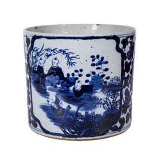 May include: A blue and white ceramic planter with a scene of children playing in a garden. The planter has a speckled glaze and a rounded shape.