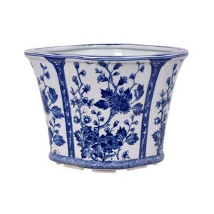 May include: A white and blue ceramic planter with a floral design. The planter has a flared shape and is decorated with blue floral patterns. The rim and base have a blue border. The overall design is classic and elegant.