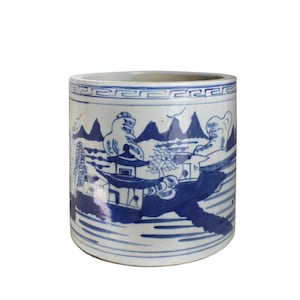 May include: A white ceramic planter with a blue and white landscape design. The planter has a cylindrical shape and a decorative border around the top.