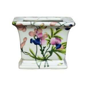 May include: White ceramic planter with a rectangular shape and a floral design. The planter features pink, blue, and green flowers with green leaves.