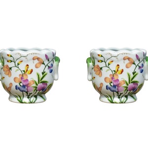 May include: Two white ceramic flower pots with green handles and floral designs in shades of pink, yellow, orange, and green.
