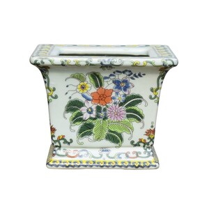 May include: A white ceramic planter with a rectangular shape and a floral design. The planter has a yellow, green, blue, orange, and pink floral pattern.