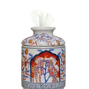 May include: A white ceramic tissue box holder with a blue and red floral design. The holder has a round shape and a lid with a small opening for tissues.