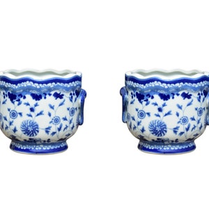 May include: Two matching white and blue ceramic planters. Each planter features a scalloped rim, blue floral patterns, and small handles. The planters have a classic, decorative design.