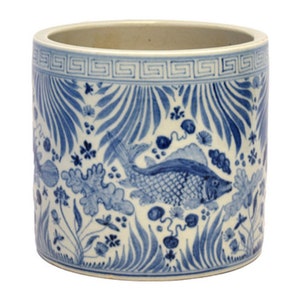 May include: A white ceramic cylinder planter with a blue and white floral and fish design. The planter has a geometric border around the top.